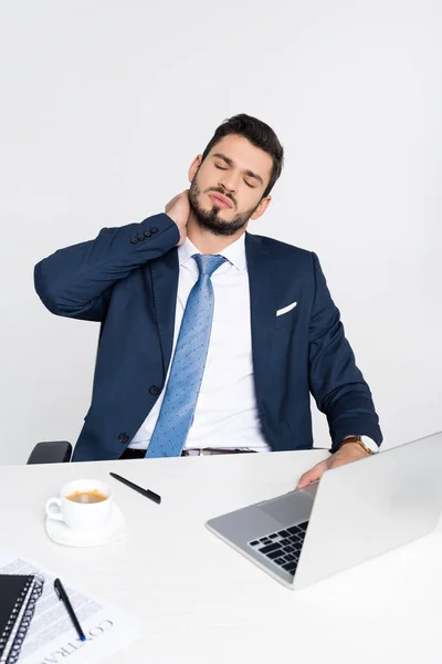 Young businessman with closed eyes suffering from pain in neck while sitting at workplace — Stock Photo