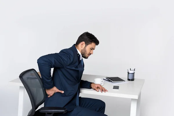 Jeune homme d'affaires souffrant de maux de dos tout en étant assis sur le lieu de travail — Photo de stock