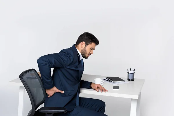 Giovane uomo d'affari che soffre di mal di schiena mentre è seduto sul posto di lavoro — Foto stock