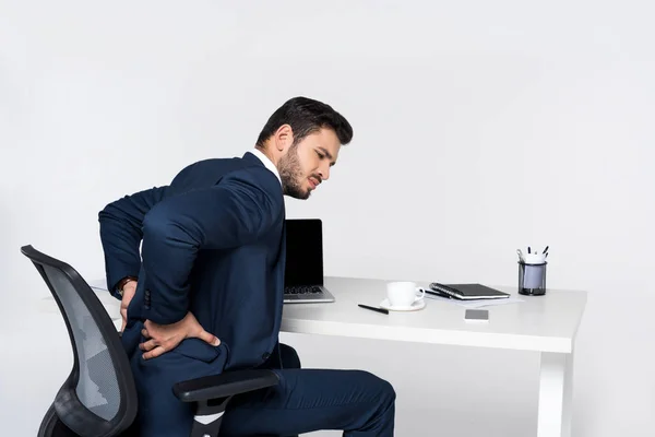 Joven empresario que sufre de dolor en la espalda mientras está sentado en el lugar de trabajo - foto de stock