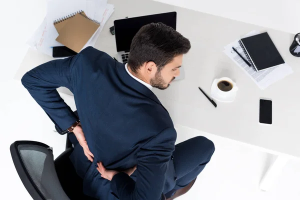 Vista de ángulo alto del joven empresario que tiene dolor de espalda mientras está sentado en el lugar de trabajo - foto de stock