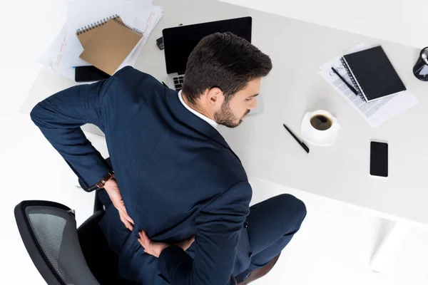 Blick aus der Vogelperspektive auf einen jungen Geschäftsmann, der am Arbeitsplatz Rückenschmerzen hat — Stockfoto