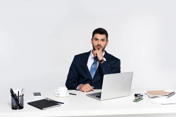 Handsome young businessman using laptop and looking at camera at workplace — Stock Photo