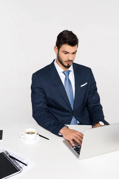 Jeune homme d'affaires concentré utilisant un ordinateur portable et boire du café sur le lieu de travail — Photo de stock