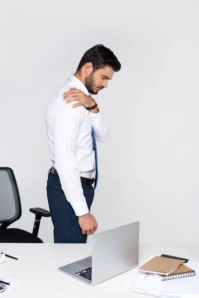 Side view of young businessman suffering from pain in shoulder while standing at workplace — Stock Photo