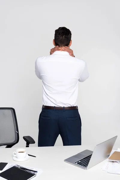 Vista posteriore del giovane imprenditore che soffre di dolore al collo mentre si trova sul posto di lavoro — Foto stock