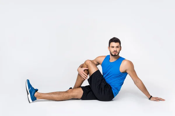 Beau jeune homme étirant la jambe tout en étant assis sur blanc — Photo de stock