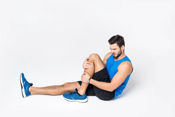 Athletic young man with pain in leg sittion on white — Stock Photo