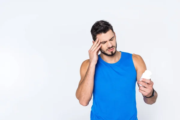 Young man with headache looking at jar of pills isolated on white — Stock Photo