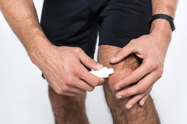 Tiro recortado del hombre aplicando ungüento en la rodilla - foto de stock