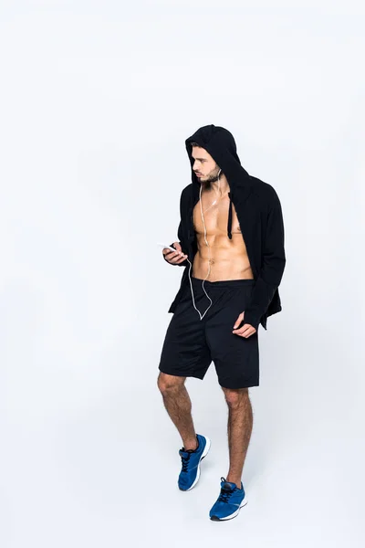 Jeune homme athlétique en sweat à capuche dézippé écoutant de la musique avec écouteurs isolés sur blanc — Photo de stock