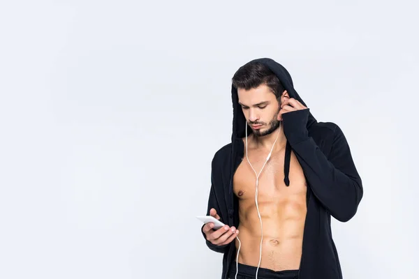 Musculoso joven con capucha desabrochada escuchando música con auriculares aislados en blanco - foto de stock