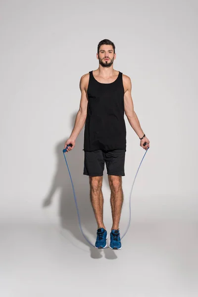 Sportive young man jumping with rope on white — Stock Photo