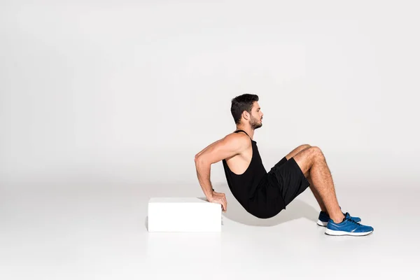 Visão lateral do jovem fazendo push-ups reversos com bloco — Fotografia de Stock