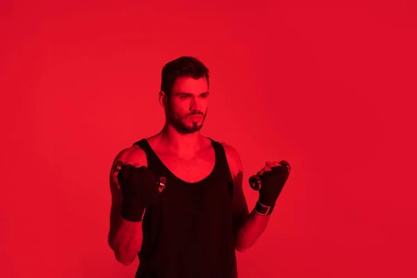 Guapo joven luchador con las manos cubiertas con vendajes bajo la luz roja - foto de stock