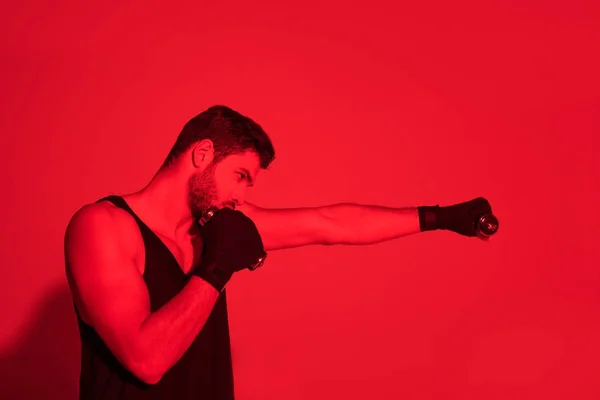 Vista lateral del luchador haciendo golpe con las manos cubiertas con vendajes bajo la luz roja - foto de stock