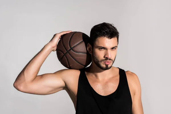 Schöner junger Basketballspieler mit Ball isoliert auf grau — Stockfoto