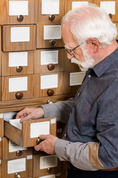 Vista lateral del archivista masculino senior en busca de catálogos - foto de stock