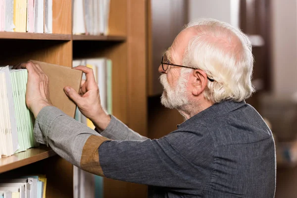 Bibliothekarin mit grauen Haaren holt Buch aus Regal — Stockfoto