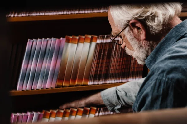 Седой волосатый библиотекарь ищет книгу — стоковое фото