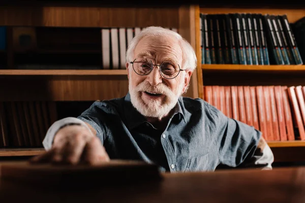 Lächelnde grauhaarige Bibliothekarin holt Buch aus dem Regal — Stockfoto