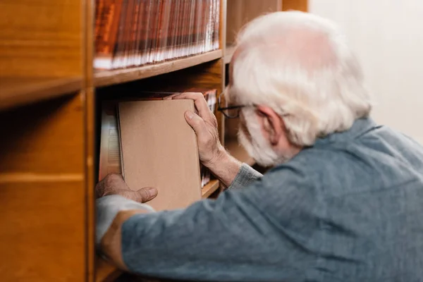 Bibliothekarin mit grauen Haaren sucht Buch im Regal — Stockfoto