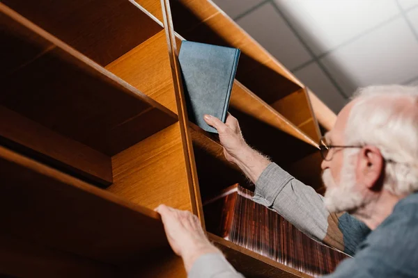 Сіре волосся бібліотекар бере книгу з полиці — стокове фото