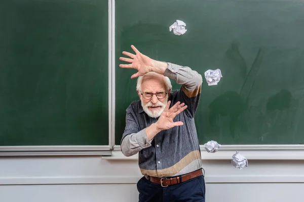 Profesor senior protegiéndose de caer pedazos arrugados de papel - foto de stock