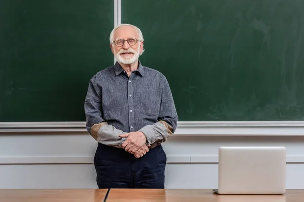 Souriant maître de conférences debout dans la salle de classe et regardant la caméra — Photo de stock