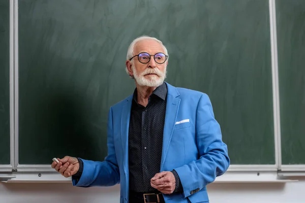 Docente senior che tiene un pezzo di gesso e distoglie lo sguardo — Foto stock