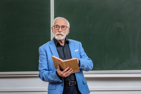 Senior lecturer holding book and looking away — Stock Photo