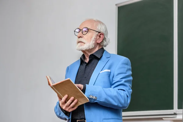 Senior Dozent hält Buch und schaut weg — Stockfoto