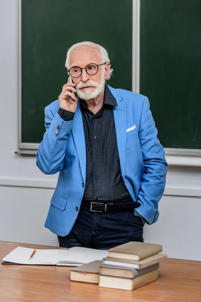 Profesor de pelo gris hablando por teléfono inteligente y mirando hacia otro lado - foto de stock