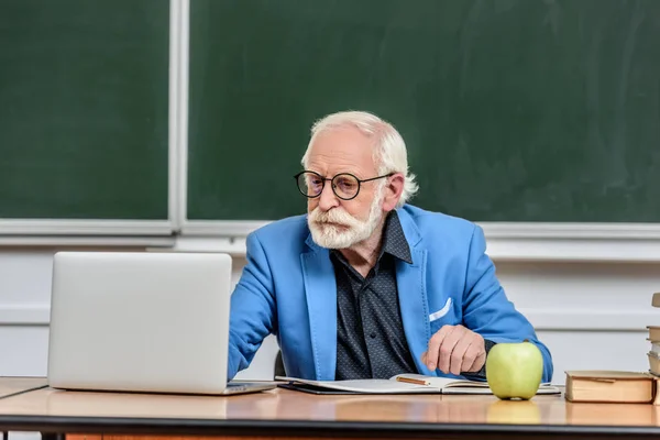 Profesor de pelo gris usando el ordenador portátil en la mesa en la sala de conferencias - foto de stock
