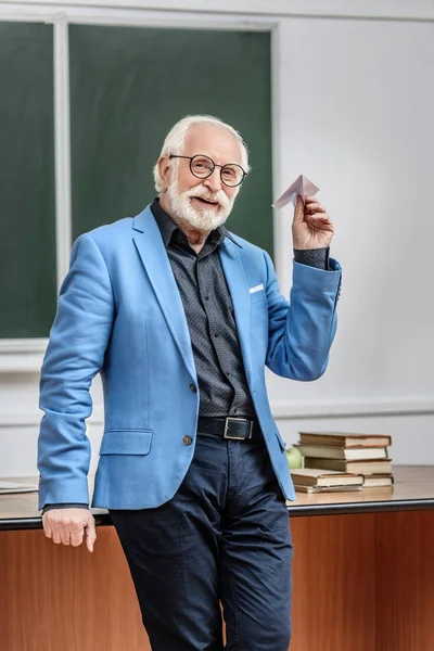 Souriant professeur de cheveux gris tenant avion en papier dans la salle de conférence — Photo de stock