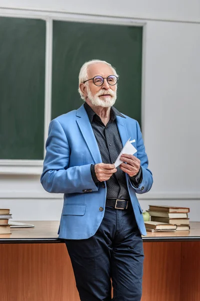 Grey hair professor holding paper plane in lecture hall — Stock Photo