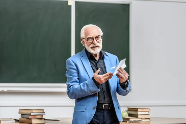 Sonriente profesor de pelo gris sosteniendo avión de papel en sala de conferencias - foto de stock