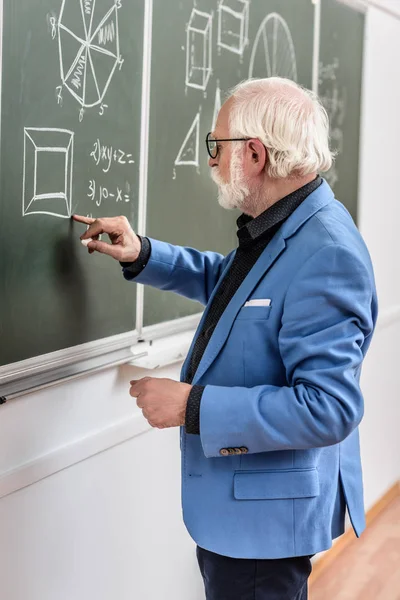 Grey hair professor correcting something at blackboard — Stock Photo