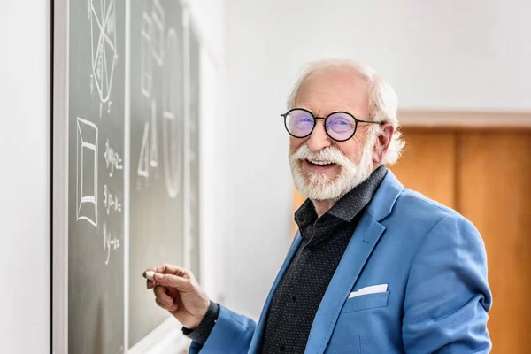 Sonriente gris profesor de pelo sosteniendo pedazo de tiza - foto de stock