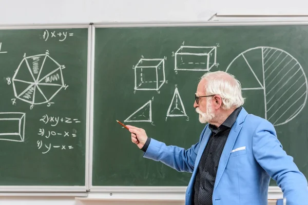 Graue Haare Professor zeigt auf etwas mit Bleistift auf Tafel — Stockfoto