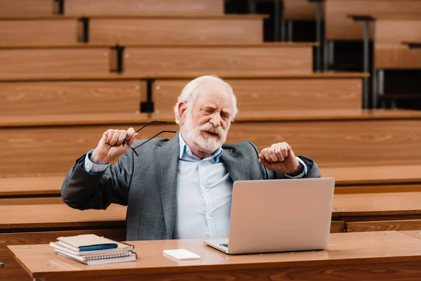 Professor de cabelo cinza esticando na sala de aula vazia — Fotografia de Stock