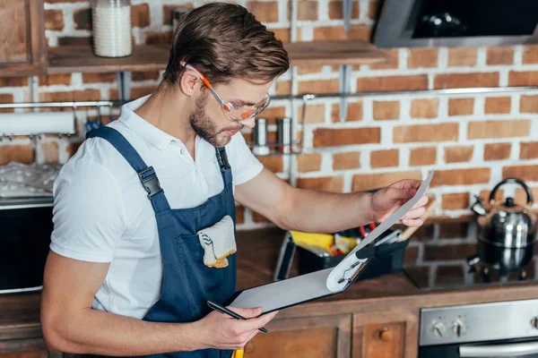 Handsome young foreman in protective workwear writing on clipboard — Stock Photo