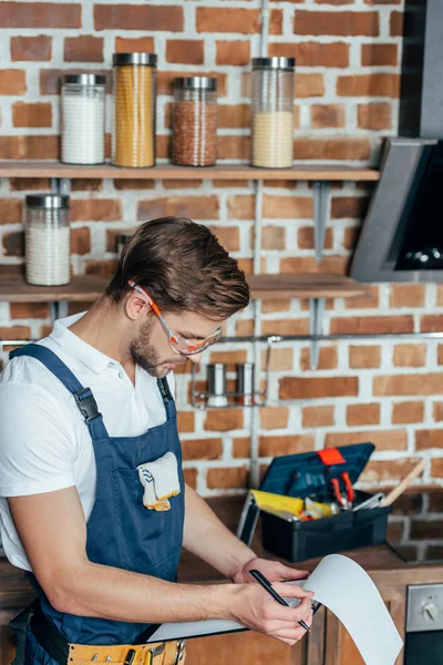 Schöner junger Reparateur, der auf Klemmbrett schreibt — Stockfoto