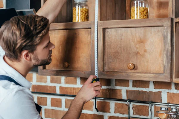 Вид збоку молодого майстра, що вимірює кухонні меблі зі стрічкою — стокове фото