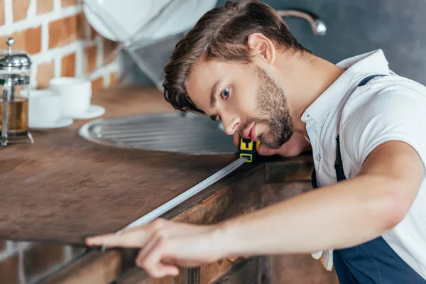 Profissional jovem faz-tudo medindo móveis de cozinha com fita — Fotografia de Stock