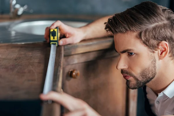 Vista de cerca de un joven capataz midiendo muebles de cocina con cinta - foto de stock