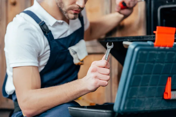 Tiro cortado de reparador segurando chave enquanto fixa o forno — Fotografia de Stock