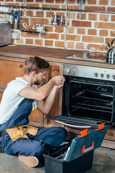 Alto angolo di vista del giovane riparatore fissaggio forno in cucina — Foto stock