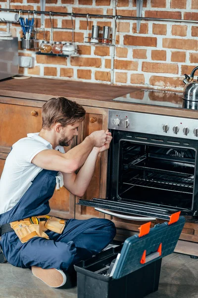 Vista de ángulo alto del joven reparador horno de fijación en la cocina - foto de stock