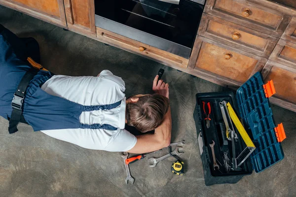 Top view of young repairman checking broken oven with flashlight — Stock Photo